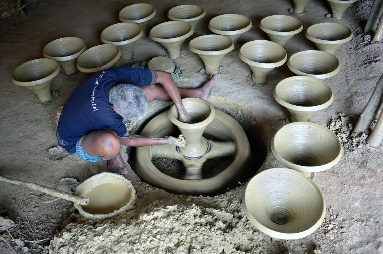 A potter at a wheel surrounded by freshly thrown bowls